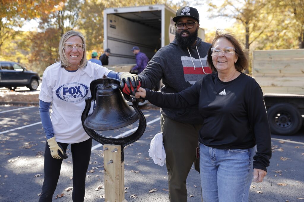 Volunteers ring bell marking completion of wheelchair ramp construction.